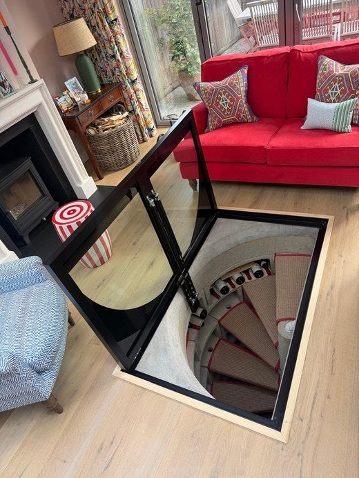 Hinged glass cellar door open on two gas struts over a spiral staircase in a London living room