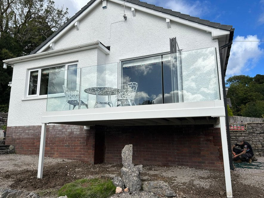 White steel balcony with frameless glass balustrade on a rendered bungalow over a sloping garden, Grange-over-Sands