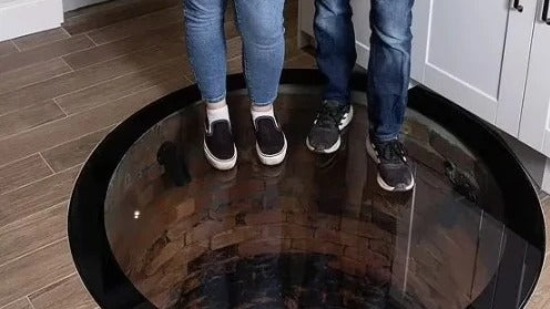 Circular walk-on glass well cover set flush into a kitchen floor, two people standing on it above a 17ft brick well, Audlem Cheshire