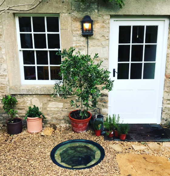 Circular walk-on glass well cover set into a gravel and stone patio in Bath