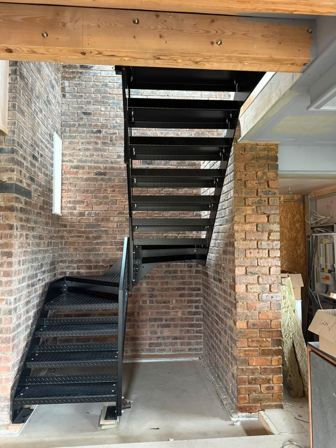 Industrial black steel staircase with Durbar chequer plate treads and welded mesh infill balustrade in a brick and beam interior