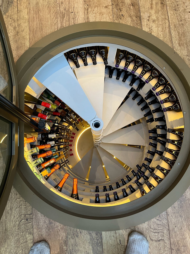 Electric circular glass floor hatch open above a spiral stair down to a wine cellar