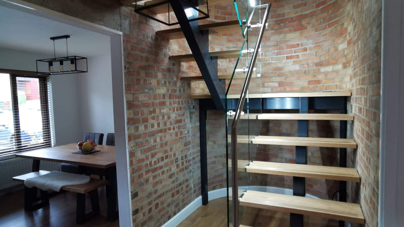 Steel spine staircase with oak treads and frameless glass balustrade against exposed brick
