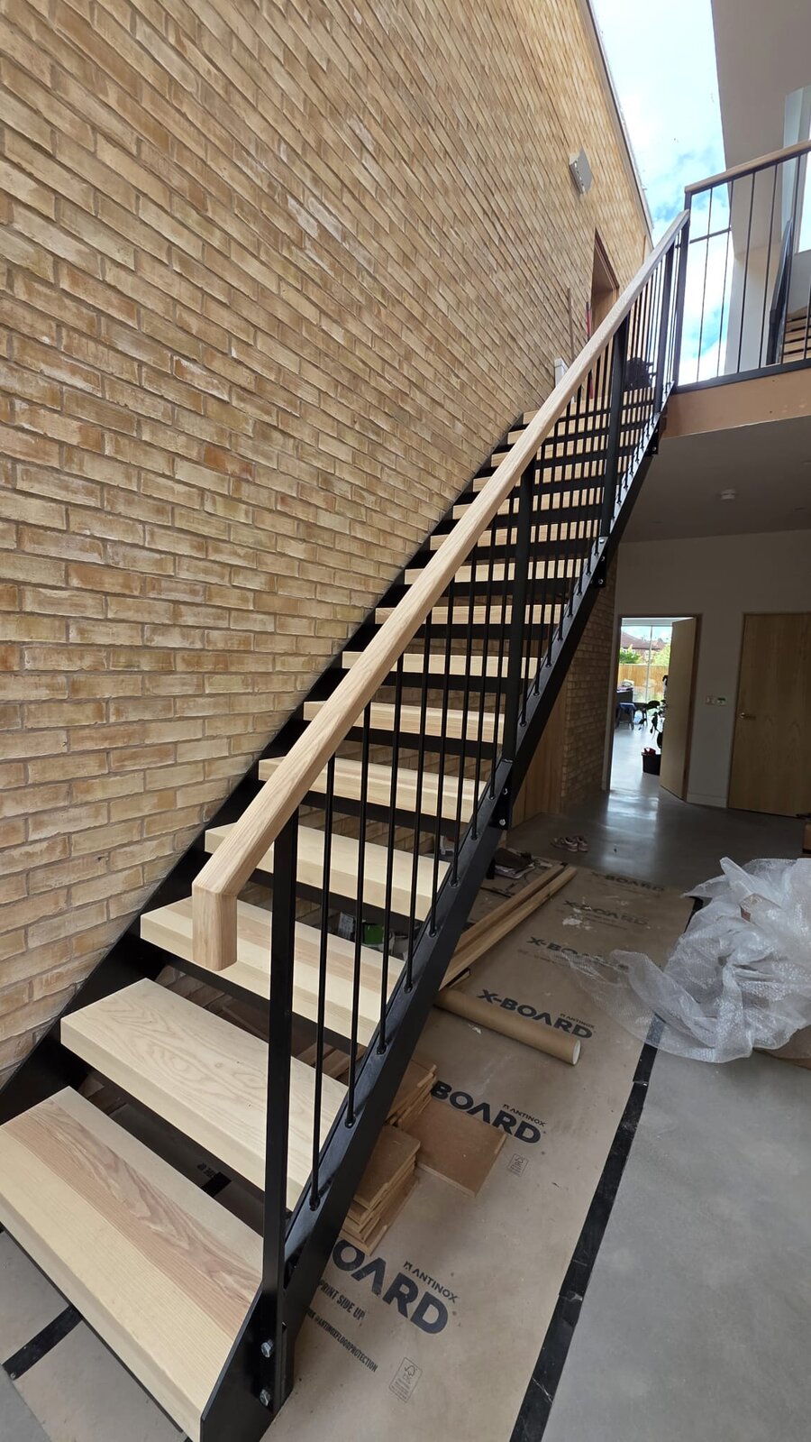Internal steel feature staircase with solid ash treads and a black powder coated metal bar balustrade