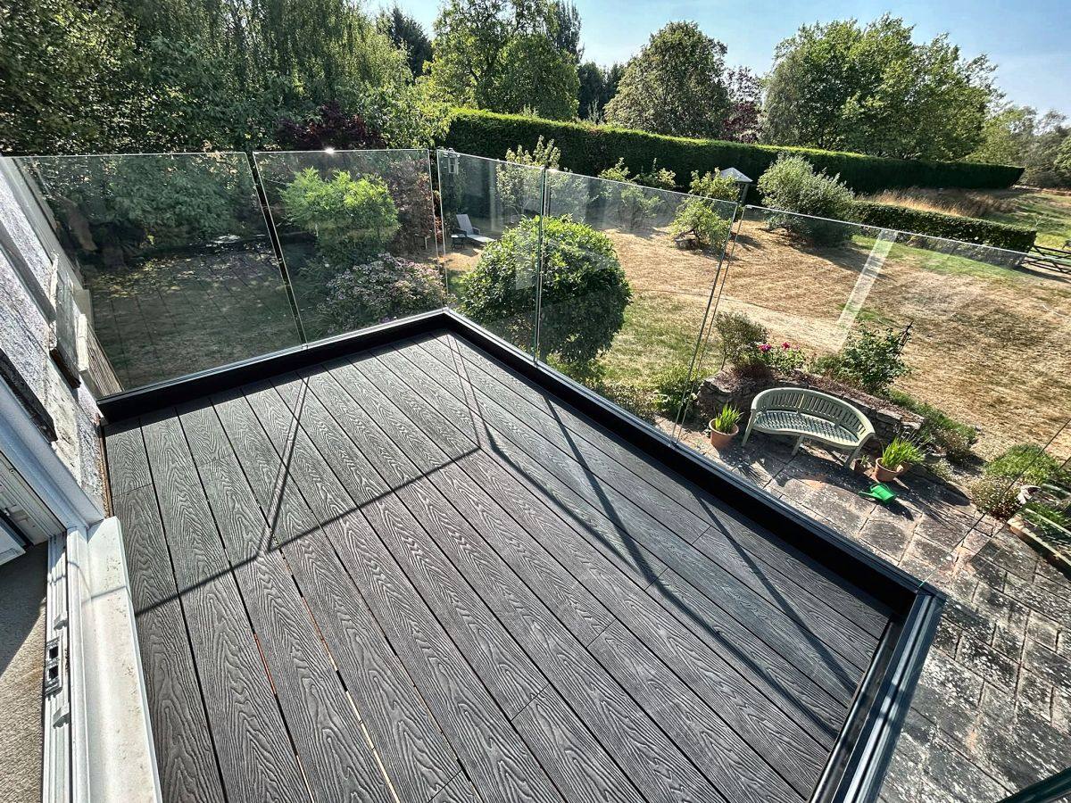View over the garden through a frameless glass balcony balustrade, Cheshire