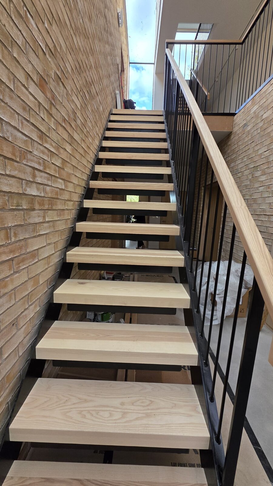 Open riser steel staircase with pale ash treads against exposed brickwork