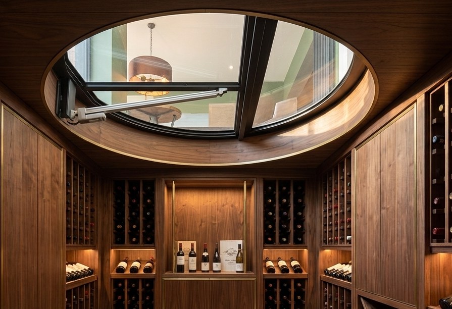 Electric circular wine cellar door open above a finished walnut wine cellar, seen from below with the actuator visible