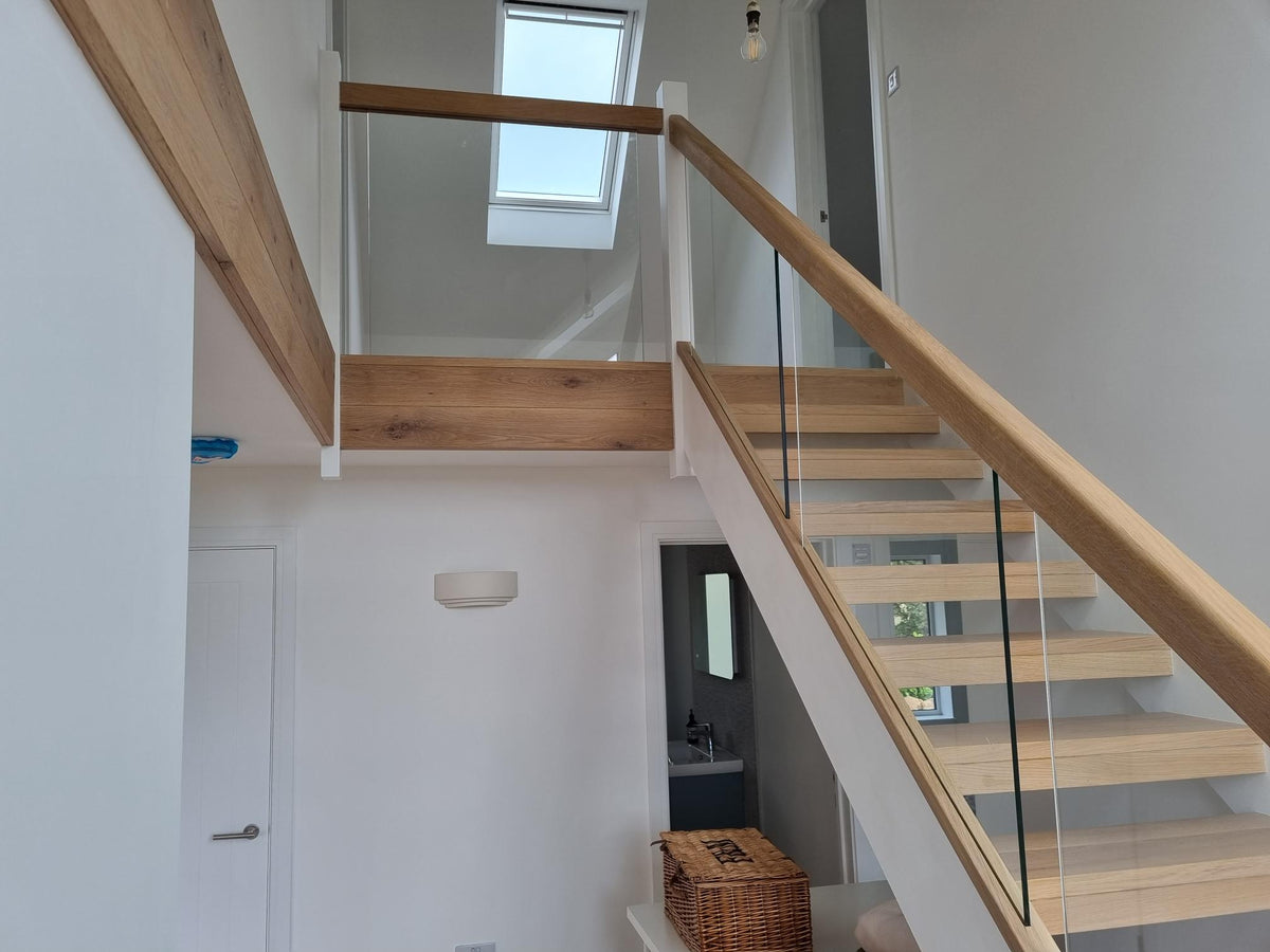 Raking glass infill panels following the pitch of an oak staircase, under an oak handrail