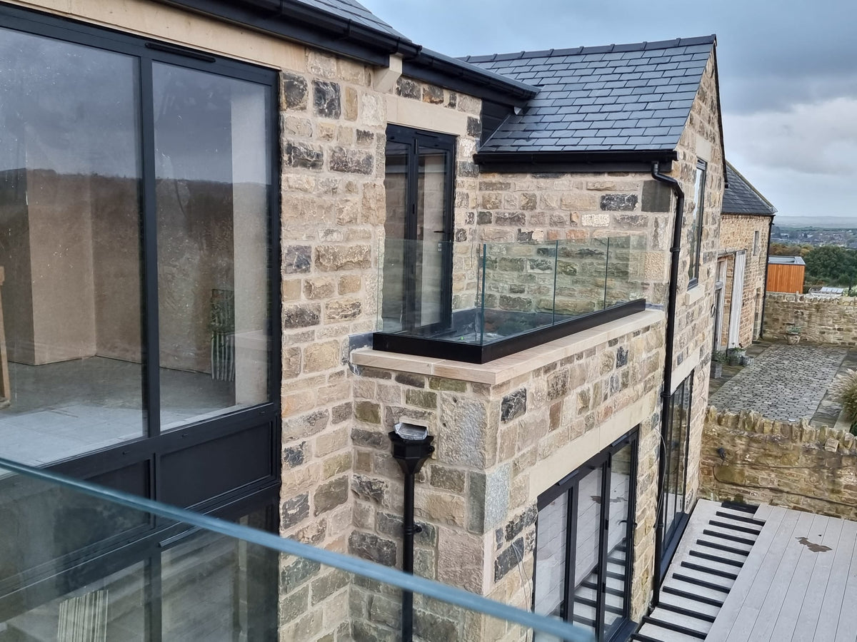 Heavy laminated glass panels in a black powder coated base channel to a stone building terrace