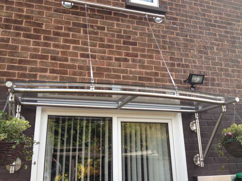 Adaptor brackets supporting a glass canopy over an entrance