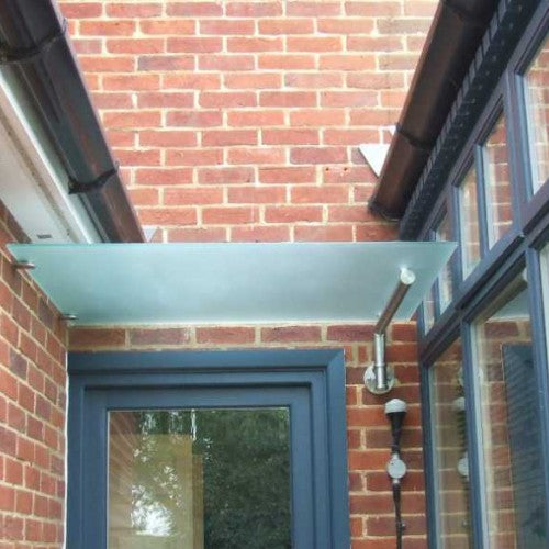 Modern glass corner canopy on stainless steel brackets over a recessed entrance