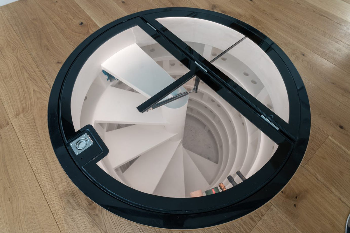 Circular glass floor hatch set into the floor above a spiral wine cellar