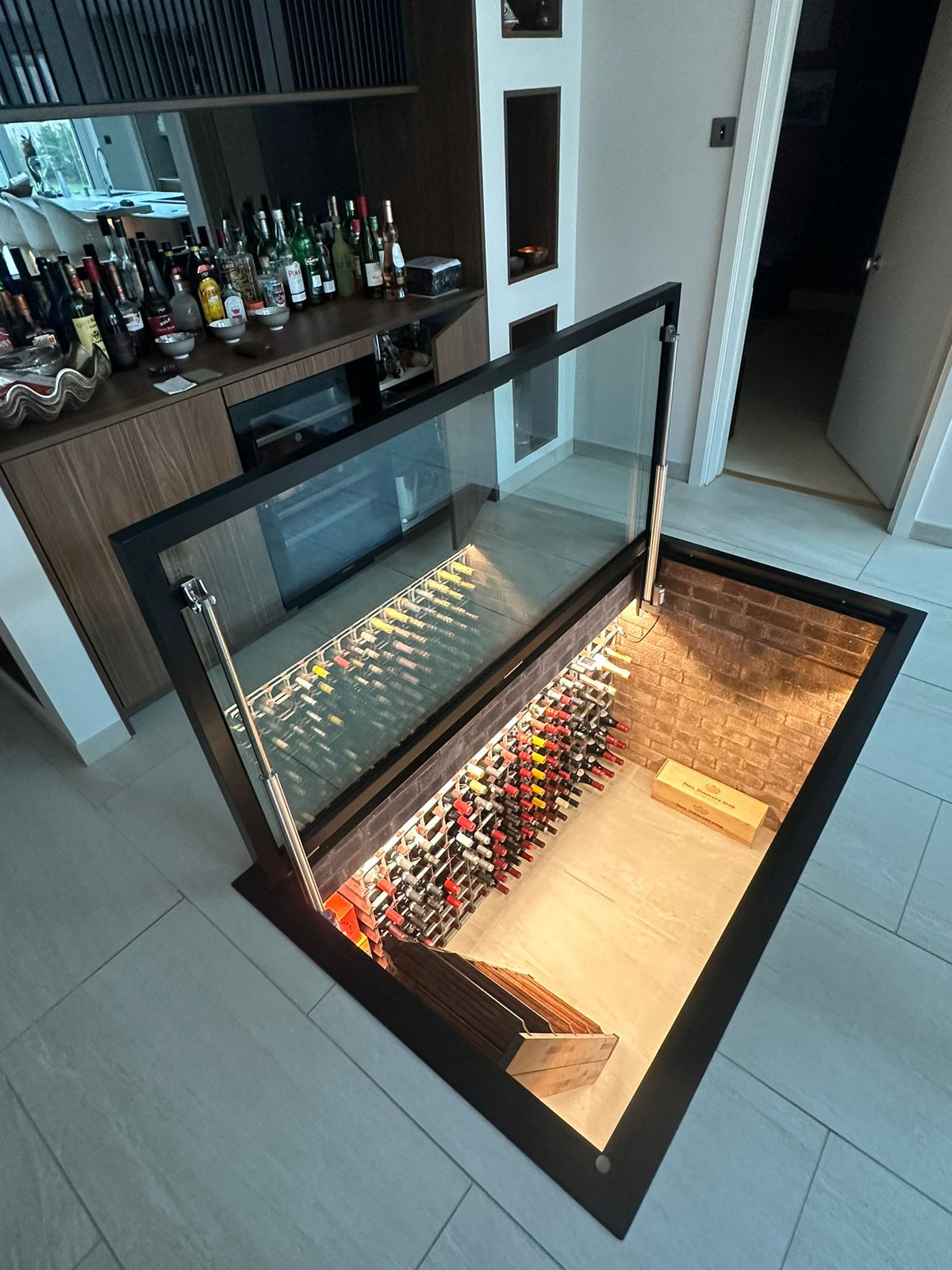 Electric glass floor hatch giving access down to a basement wine cellar