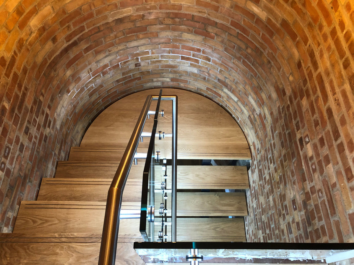 Looking down a modern steel and glass staircase under a brick vaulted ceiling