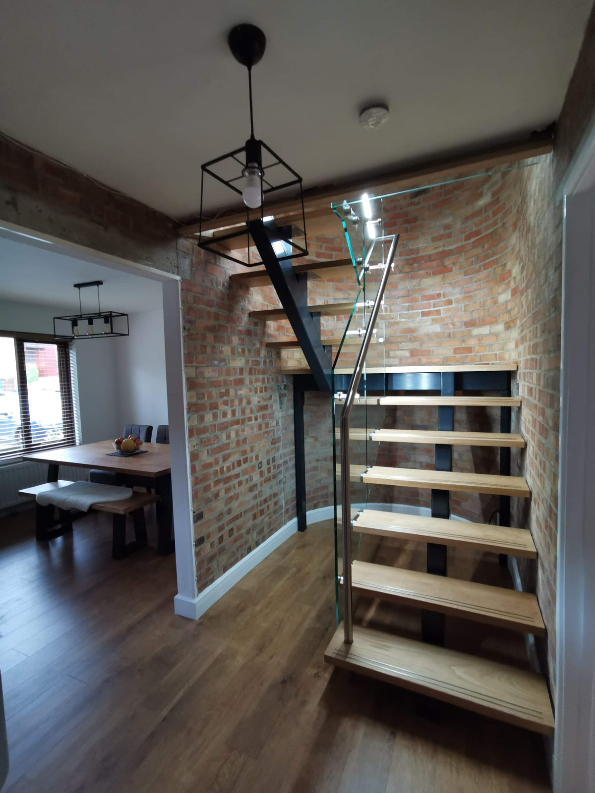 Floating steel spine staircase with oak treads and frameless glass balustrade against exposed brick