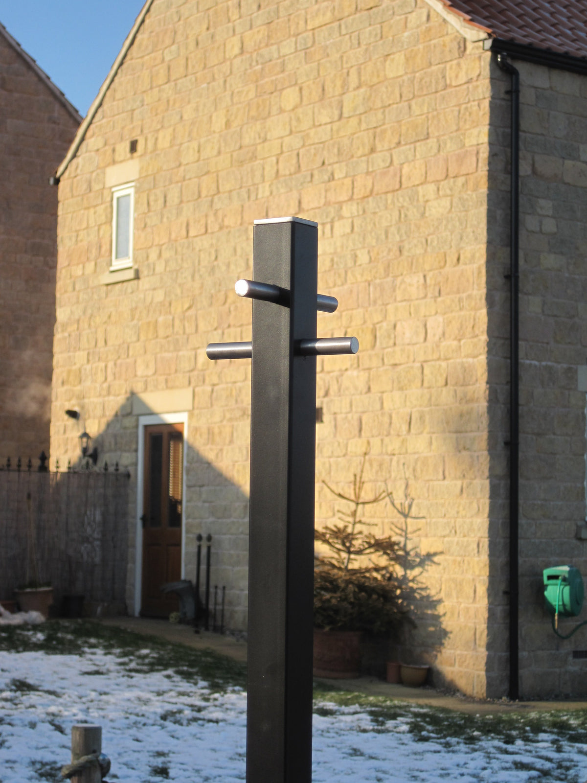 Modern square section washing line pole installed in a garden beside a stone house