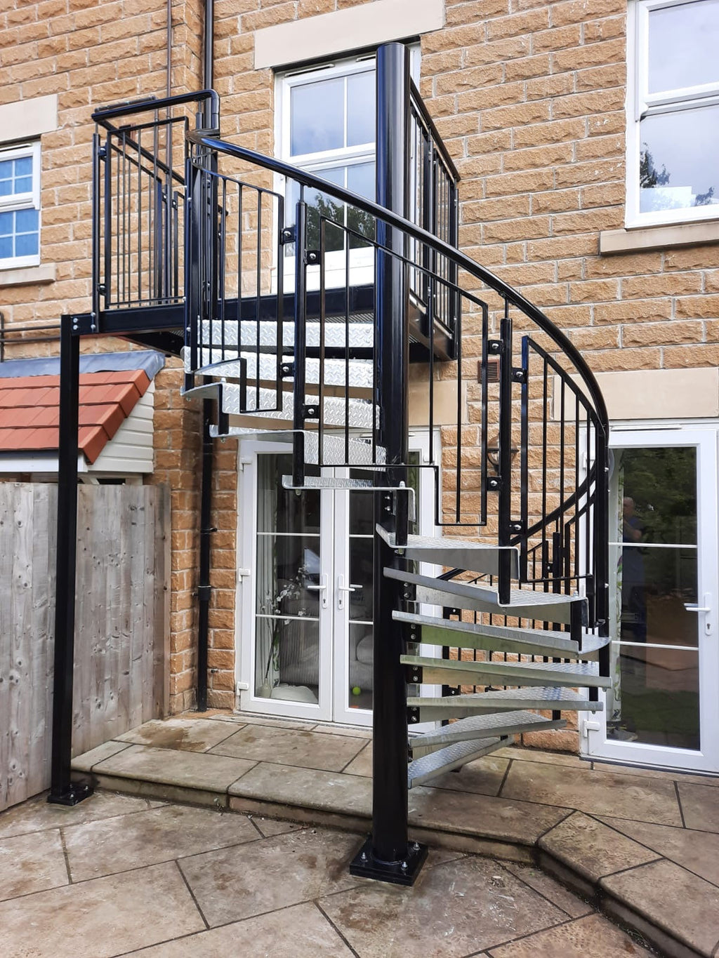 Black powder coated external steel spiral staircase on a stone house