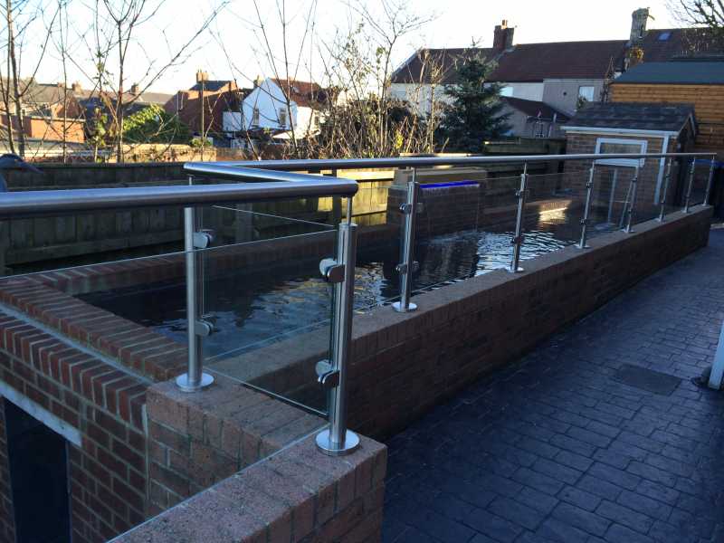 Brushed stainless steel glass balustrade on a balcony with top mounted baluster base plates
