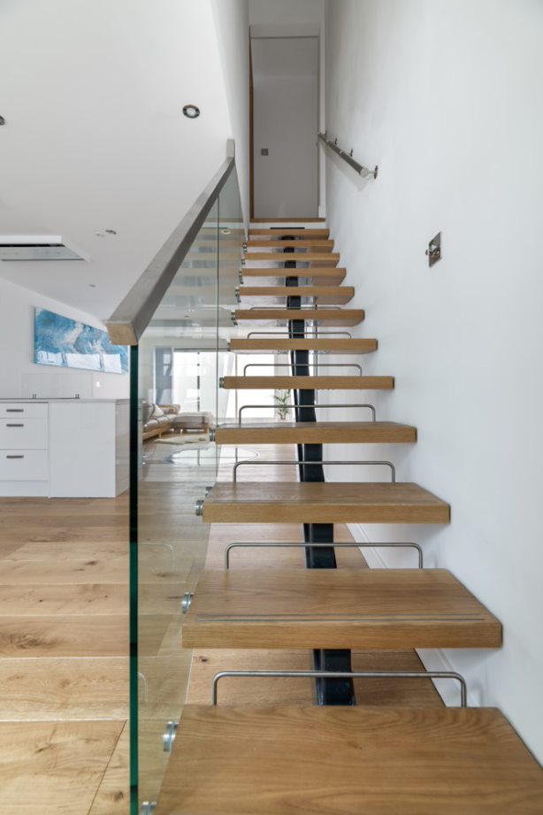 Stainless metal riser bars between the oak treads of a steel spine staircase