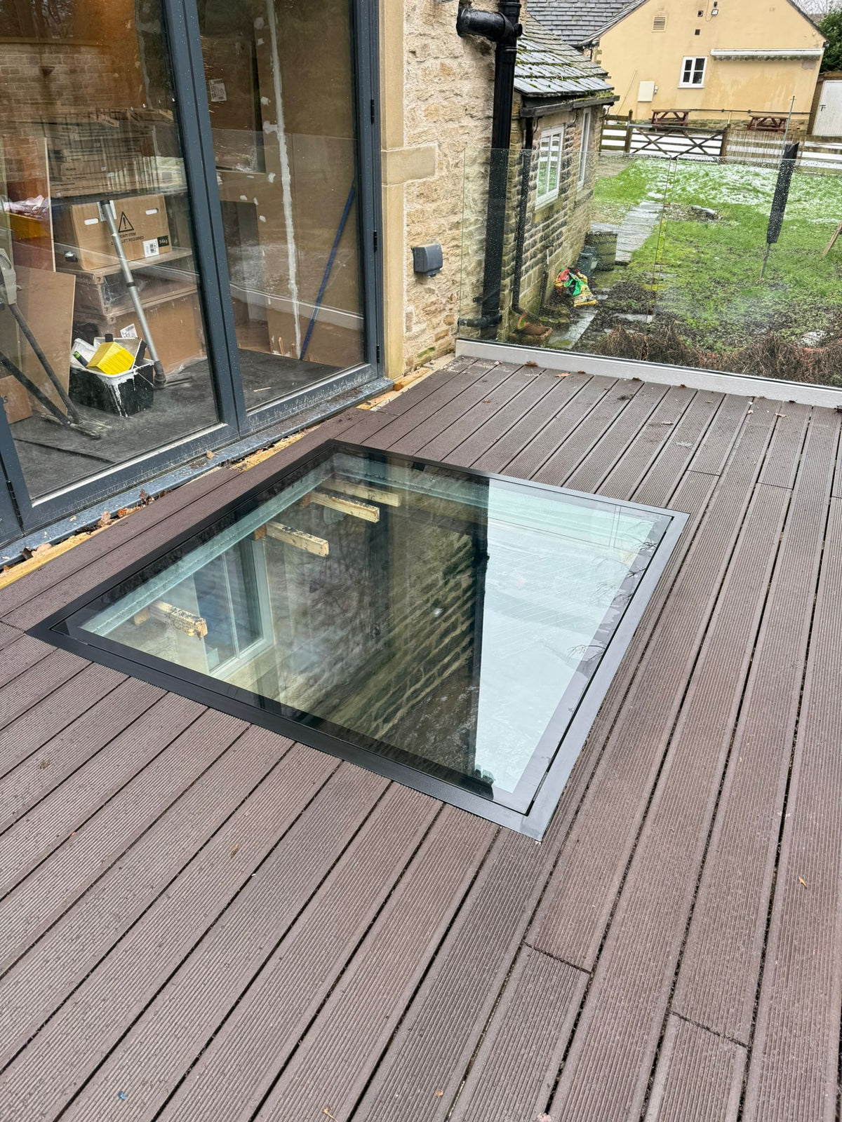 Walk-on glass floor panel in a black steel frame set into composite decking