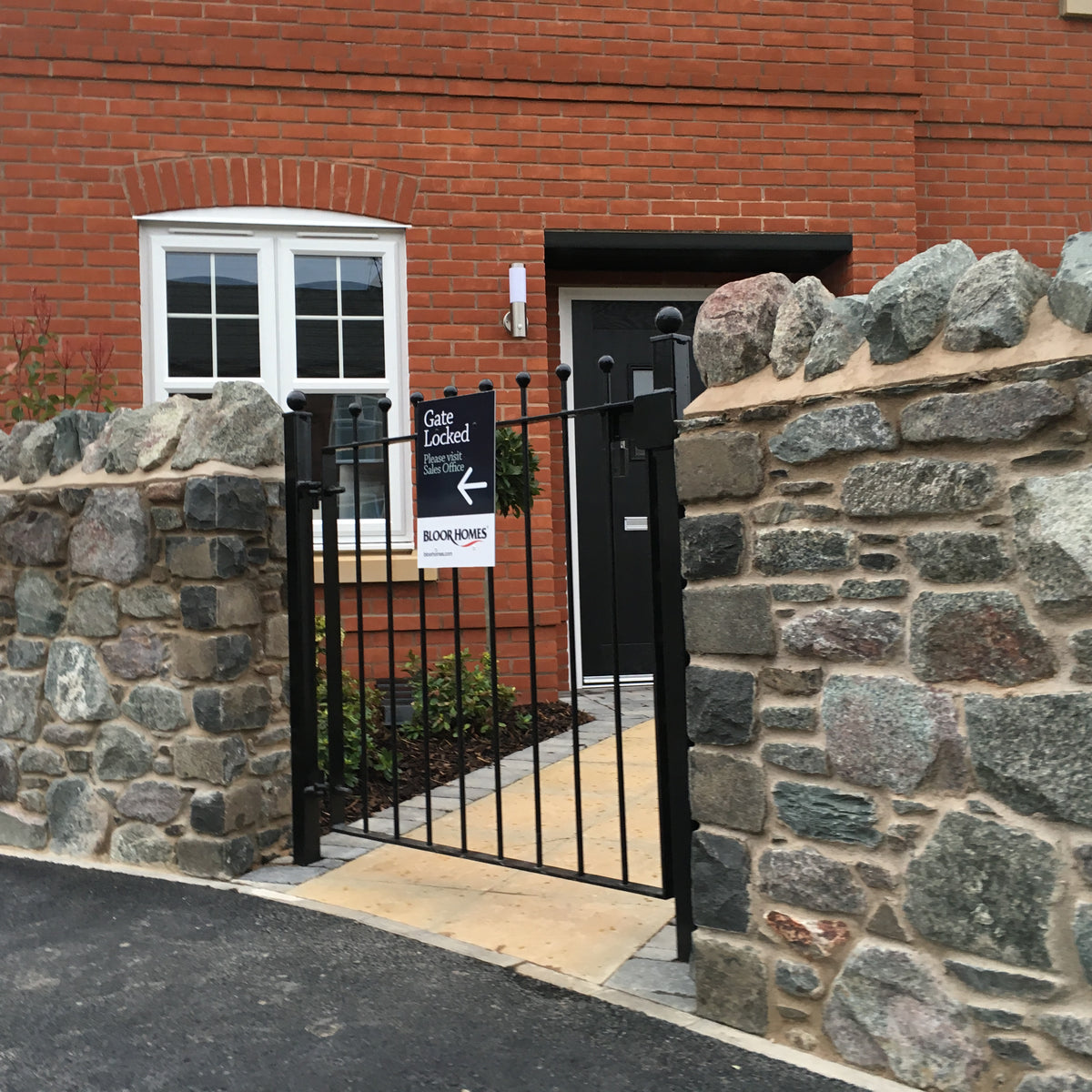 Ball top metal gate between stone piers on its own hinge and latch posts, galvanised and powder coated black