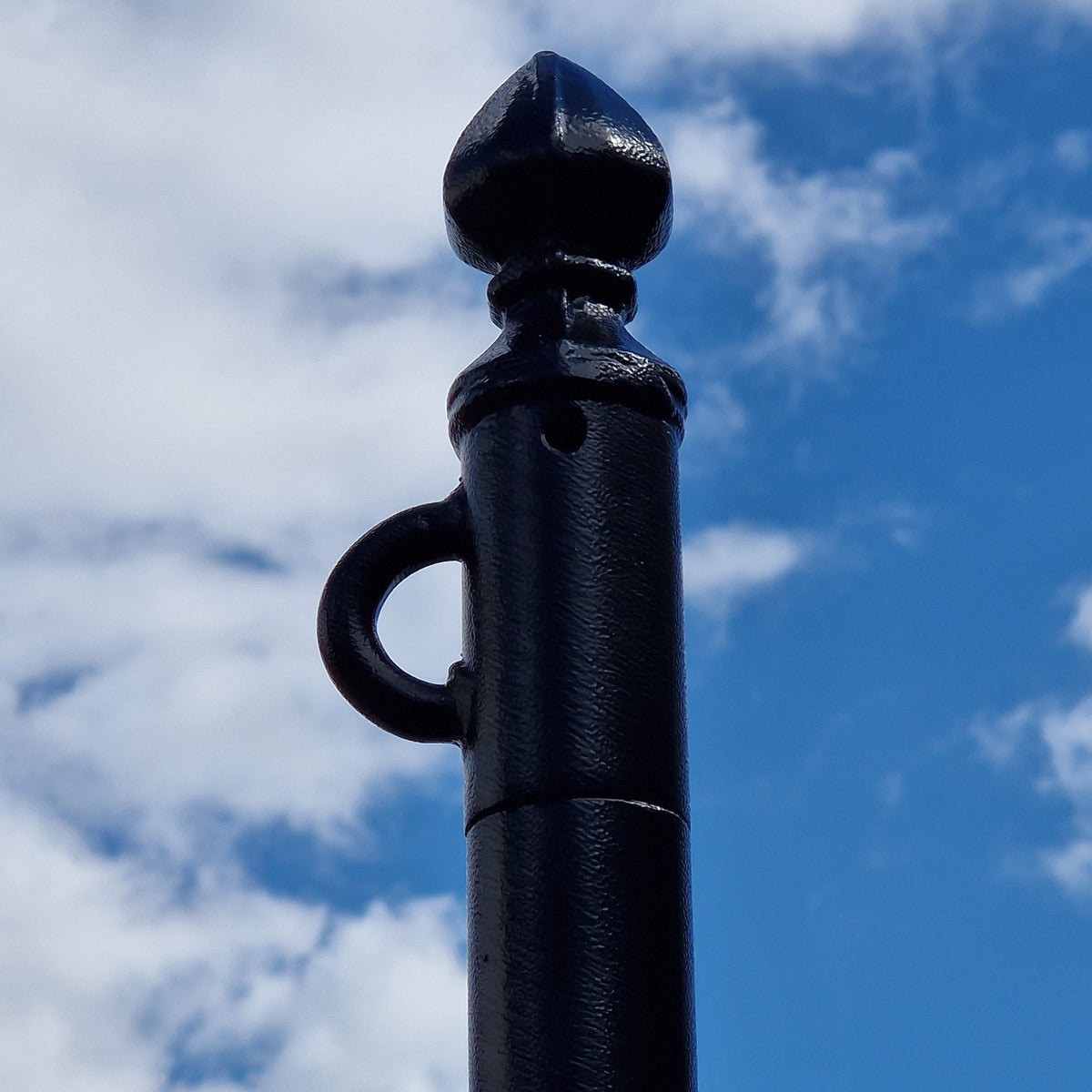 Welded loop and ornate cap on a black powder coated washing line pole against a blue sky