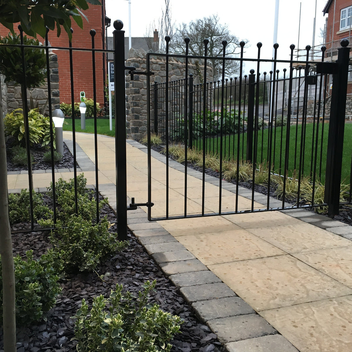 Black powder coated ball top metal gate hung in a matching ball top railing run on a front path