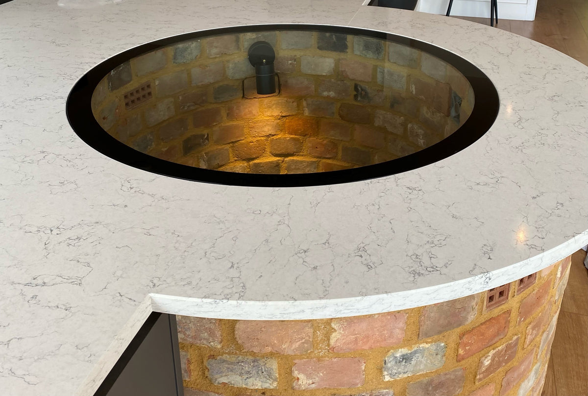 Large circular walk-on glass well cover over a brick well in a paved courtyard