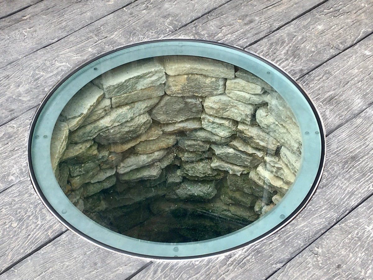 Walk-on glass well cover set into timber decking, looking down into the original stone well