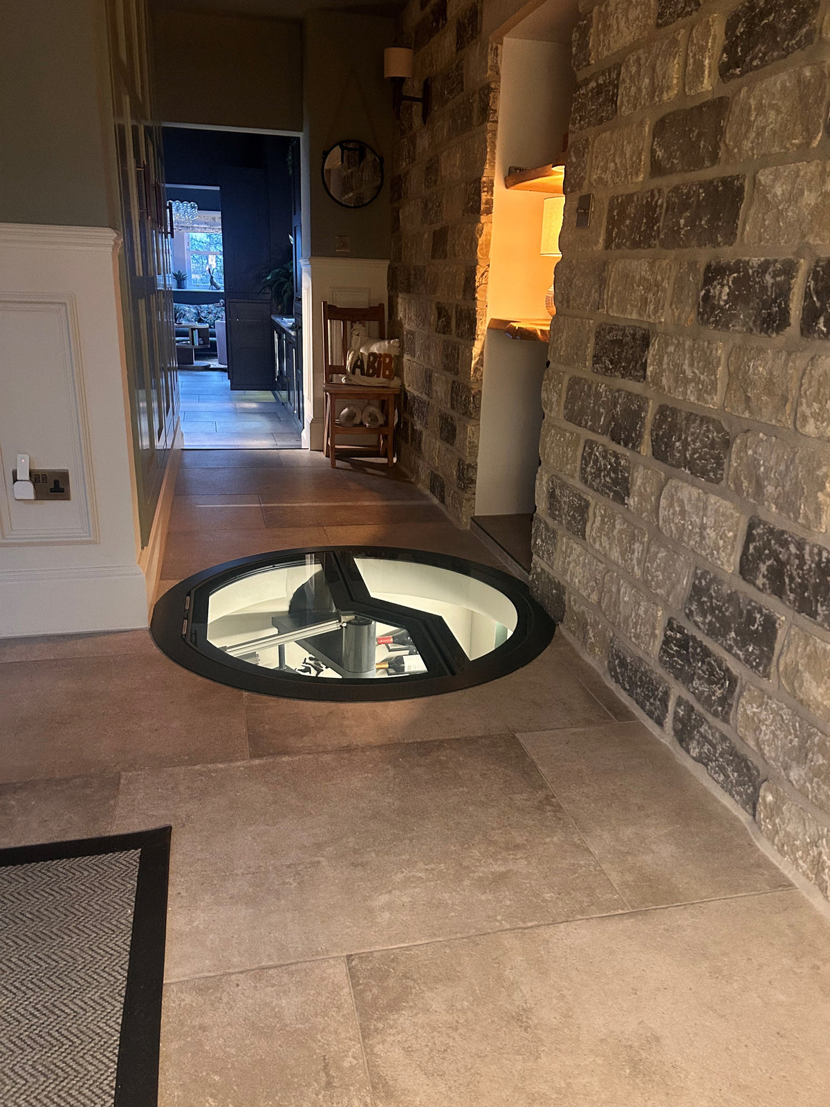 Circular glass floor hatch over a spiral stair, opened by electric actuator