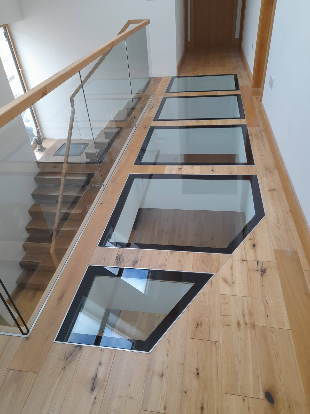 Shaped 31.5mm walk-on glass floor panels in steel frames set into an oak landing