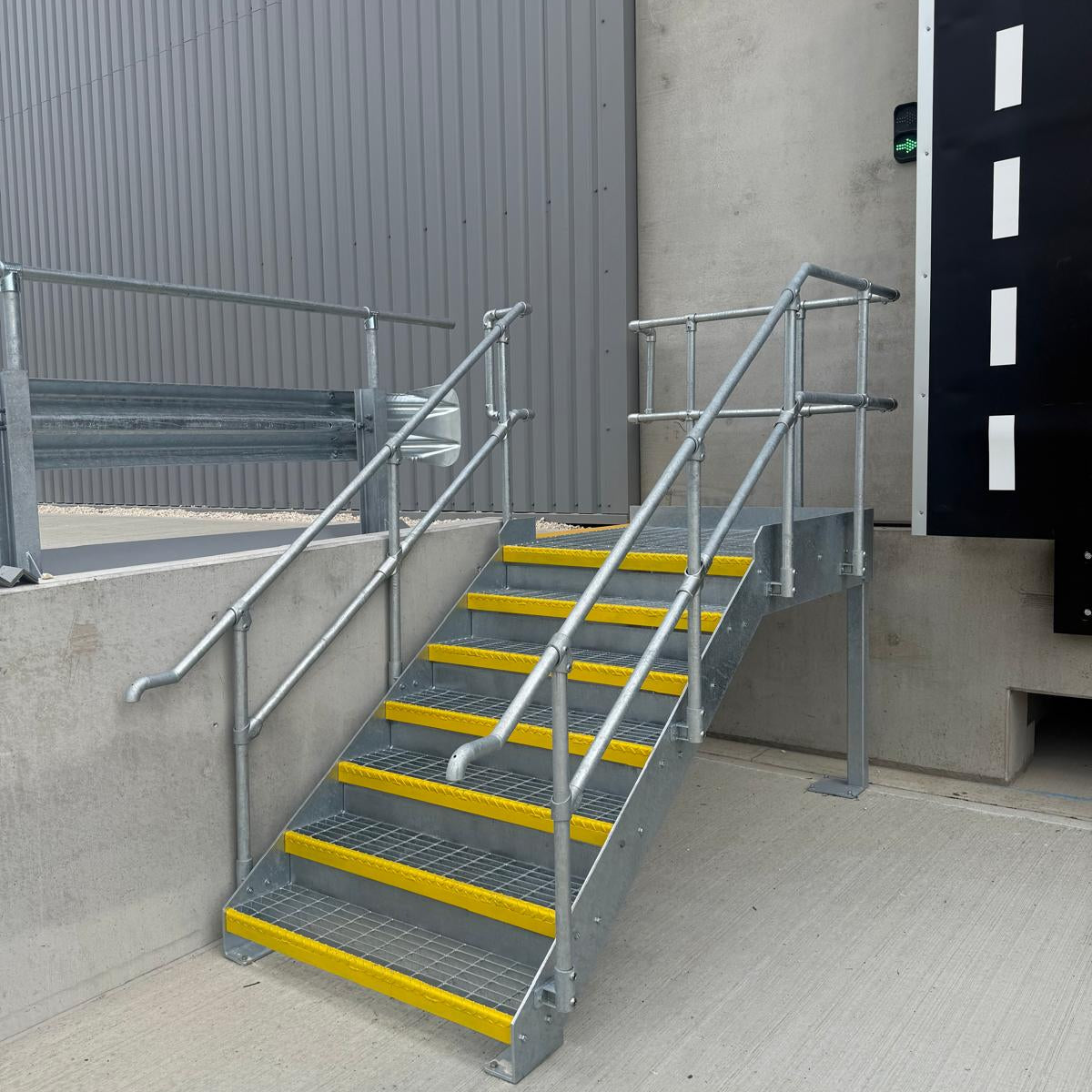 Galvanised steel access staircase to a loading dock, with open mesh treads, yellow safety nosings and key clamp handrails