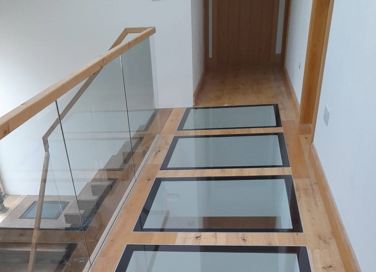 Walk-on glass floor panels in steel frames beside a glass balustrade on an oak landing