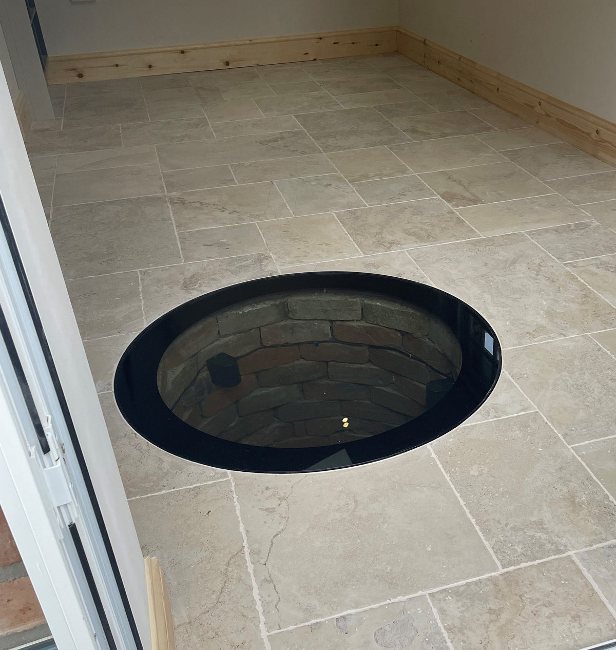 Circular glass well cover in a steel frame set into a tiled floor over a stone well