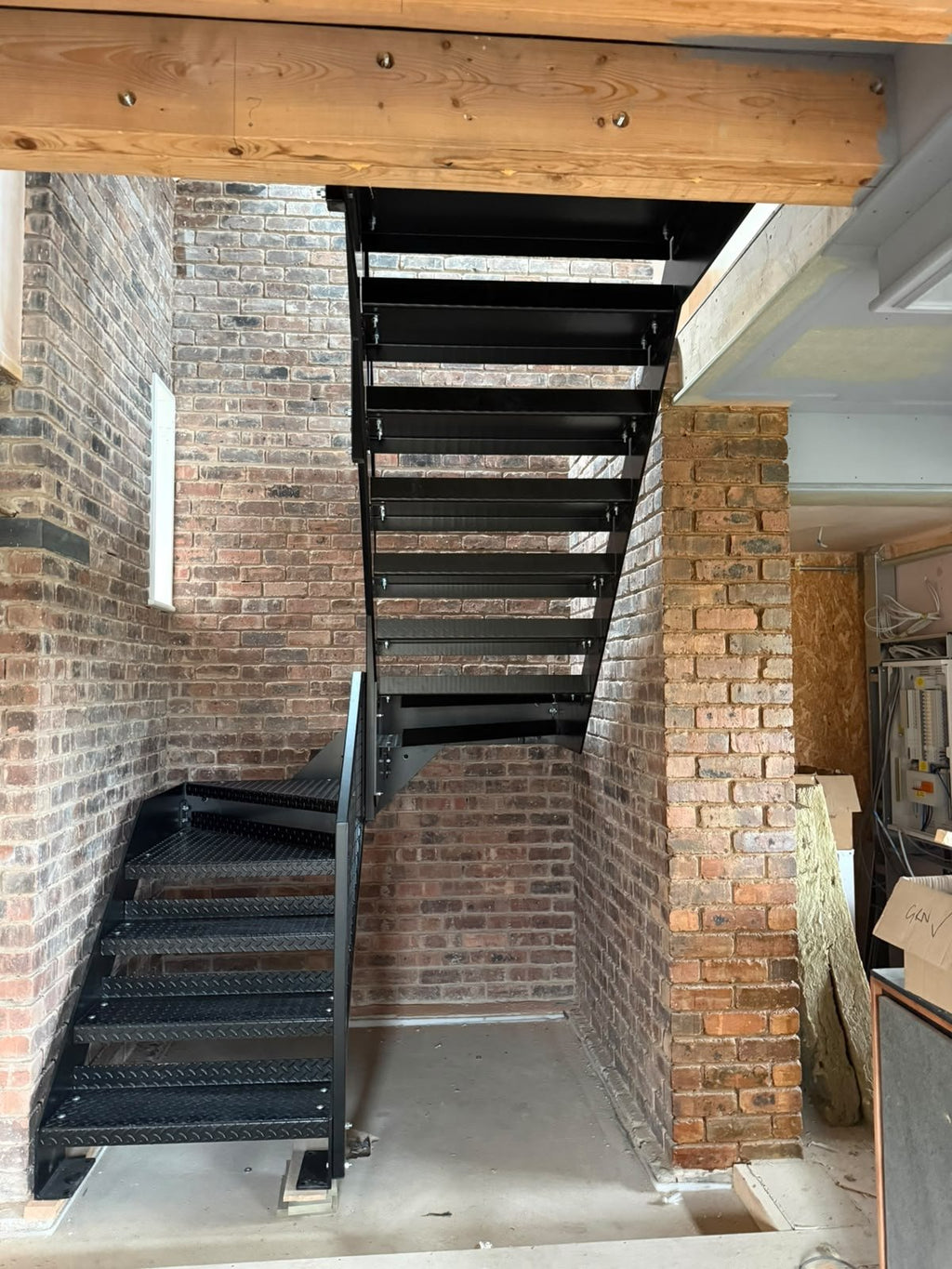 Industrial black steel staircase with Durbar chequer plate treads and welded mesh infill balustrade in a brick and beam interior