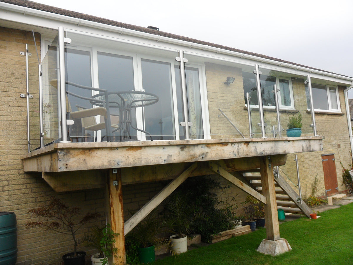 Laminated glass balustrade panels in side fixed clamps to a raised timber deck