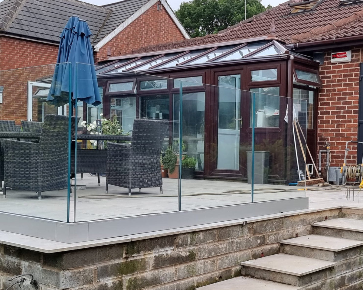Laminated glass patio balustrade with no top rail above a stone retaining wall