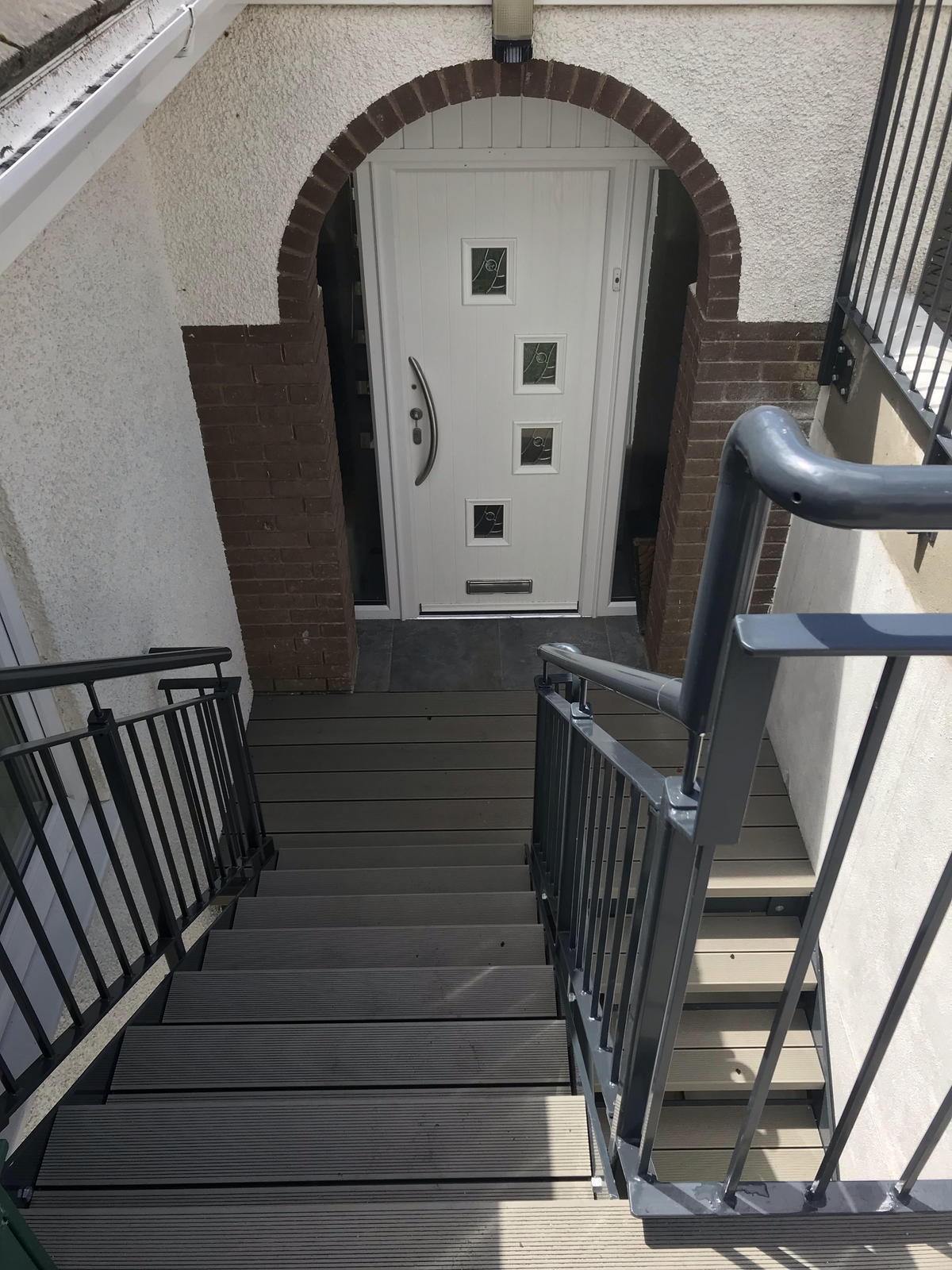Black powder coated steel staircase with bar infill metal railings to a front door