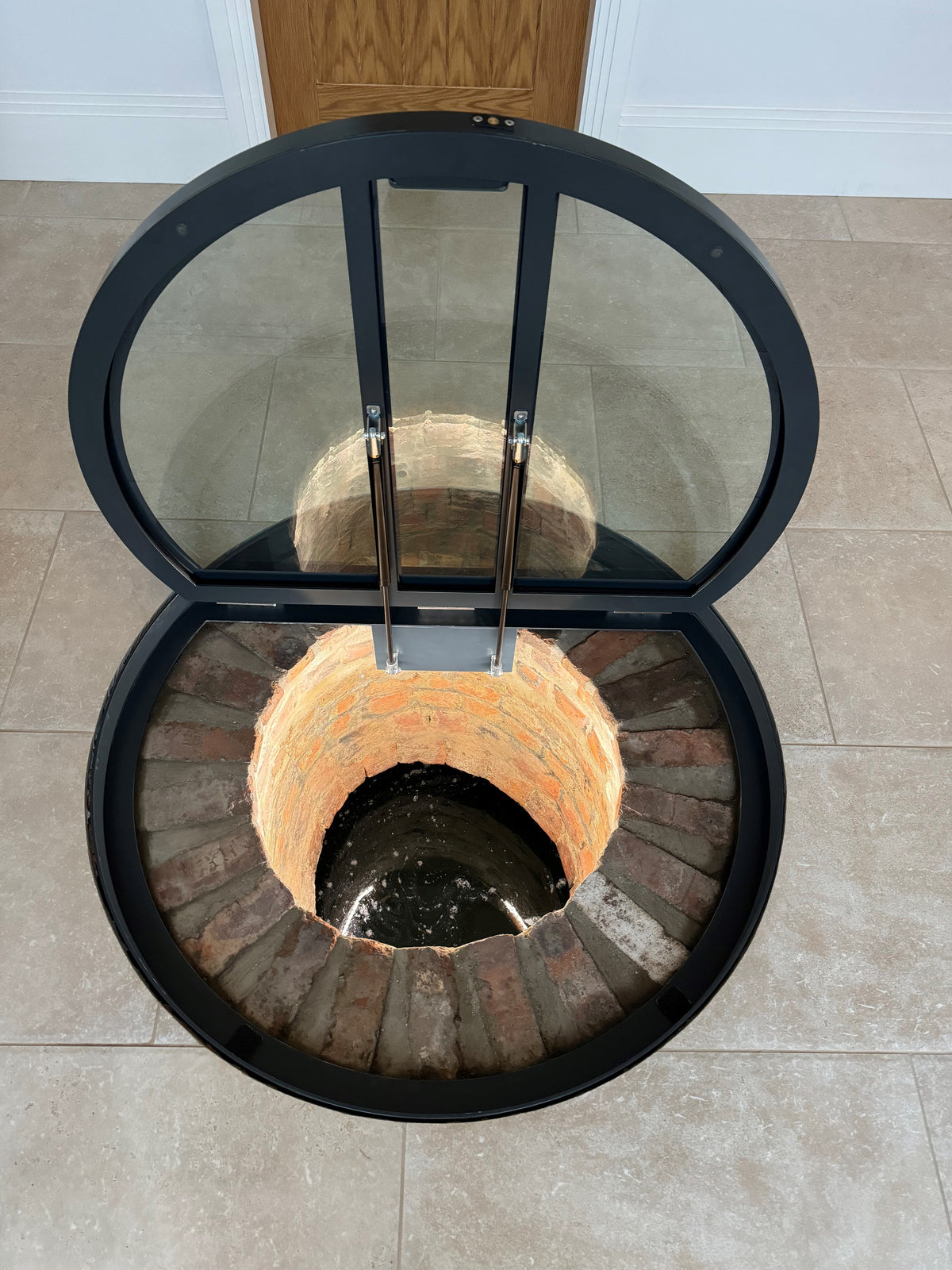 Openable glass floor door over a circular well opening