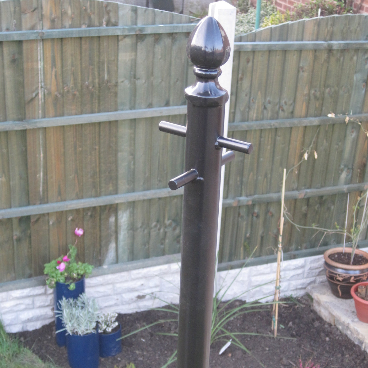 Ornate washing line pole powder coated black, installed in a garden border beside a fence