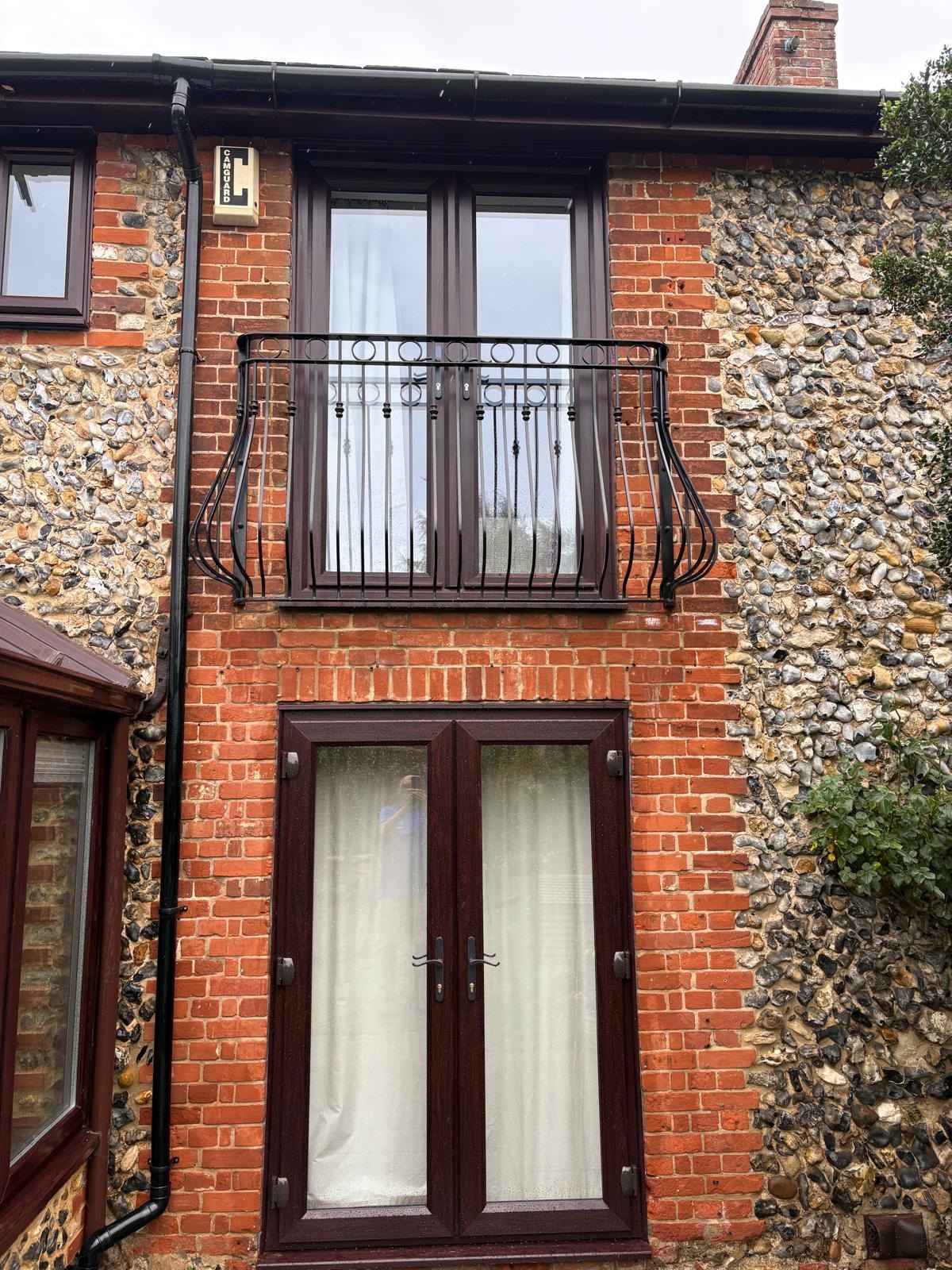 Regency ornate steel Juliet balcony in black on a brick and flint cottage