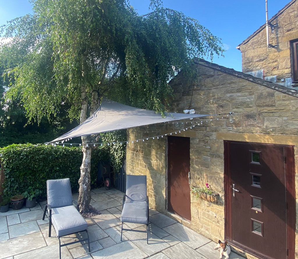 Grey shade sail rigged over a garden seating area on steel posts