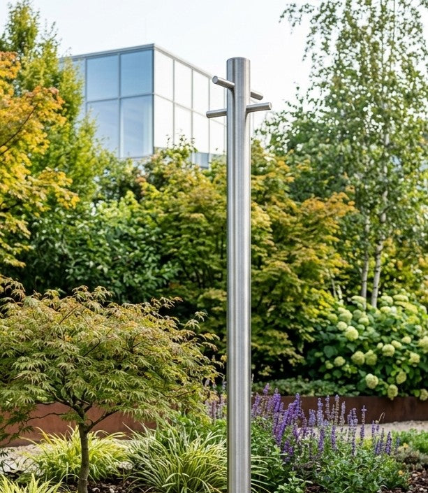 Brushed stainless steel washing line pole installed in a landscaped garden with planting behind