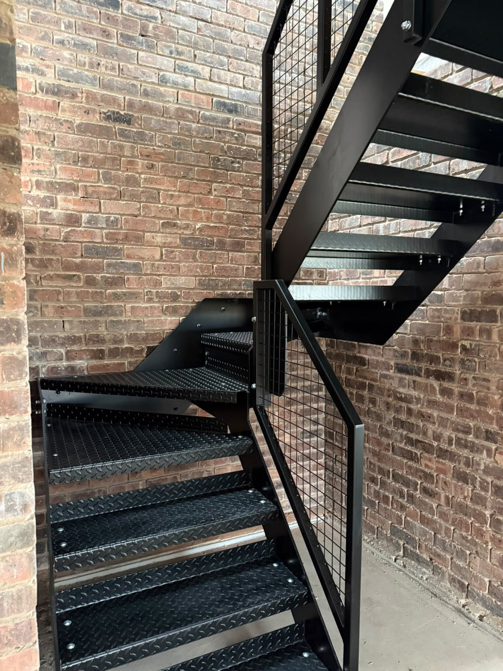 Underside of a steel staircase showing the 220 x 10mm plate stringers and angle cleats carrying each tread