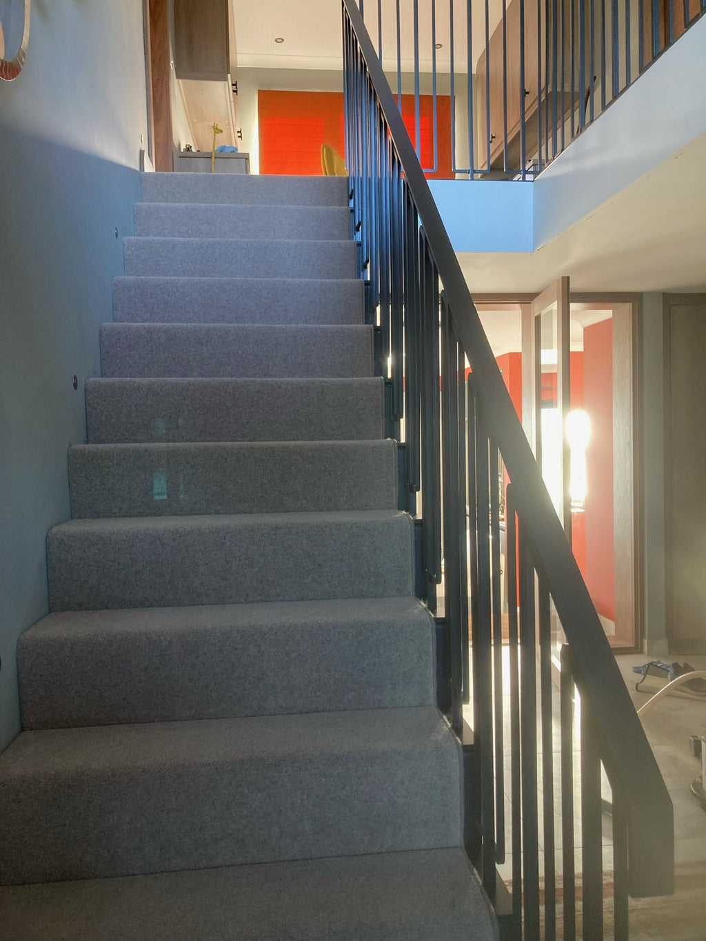 Steel staircase with carpeted treads and a black metal balustrade with rectangular loop balusters
