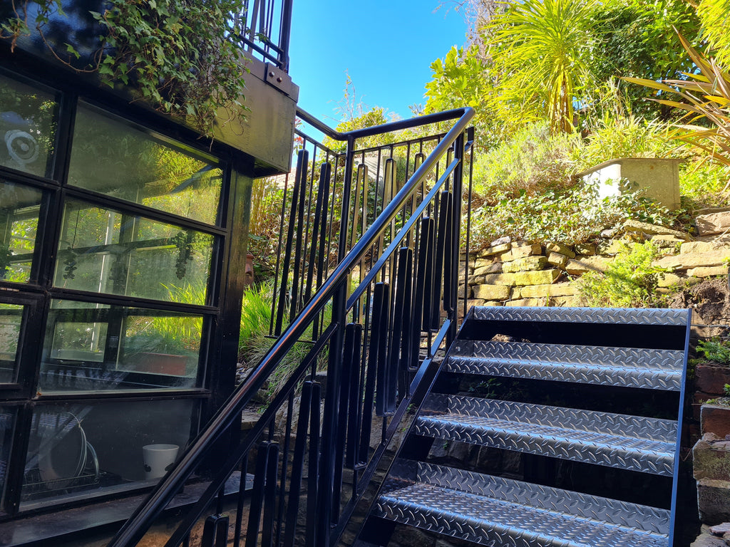 Powder coated steel staircase with custom metal railings beside a garden room