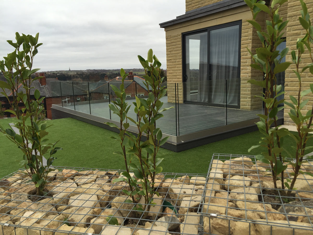 Frameless glass balustrade in a base channel around a raised terrace on a stone house