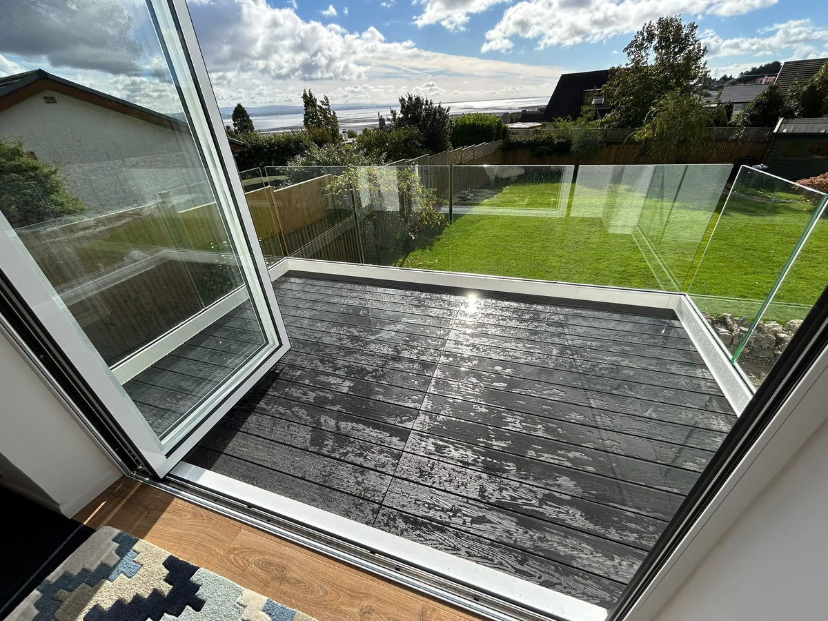Looking out from first floor sliding doors onto a composite decked balcony with a frameless glass balustrade